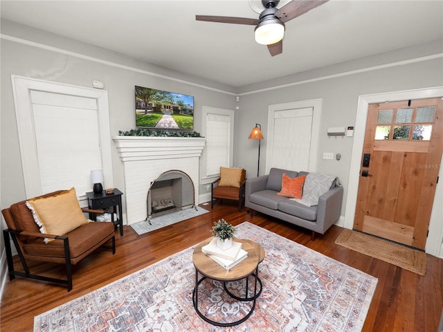 living room featuring ceiling fan, a brick fireplace, and wood finished floors