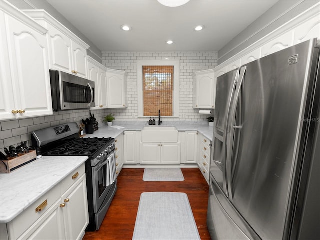 kitchen featuring tasteful backsplash, dark wood-style flooring, stainless steel appliances, white cabinetry, and a sink