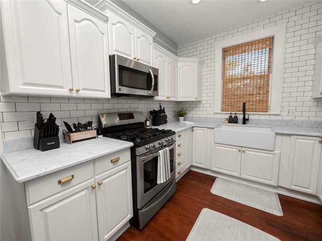 kitchen with dark wood-type flooring, a sink, white cabinets, appliances with stainless steel finishes, and tasteful backsplash