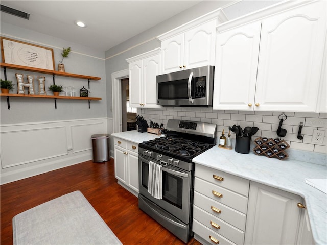 kitchen with dark wood-style flooring, backsplash, appliances with stainless steel finishes, white cabinetry, and wainscoting