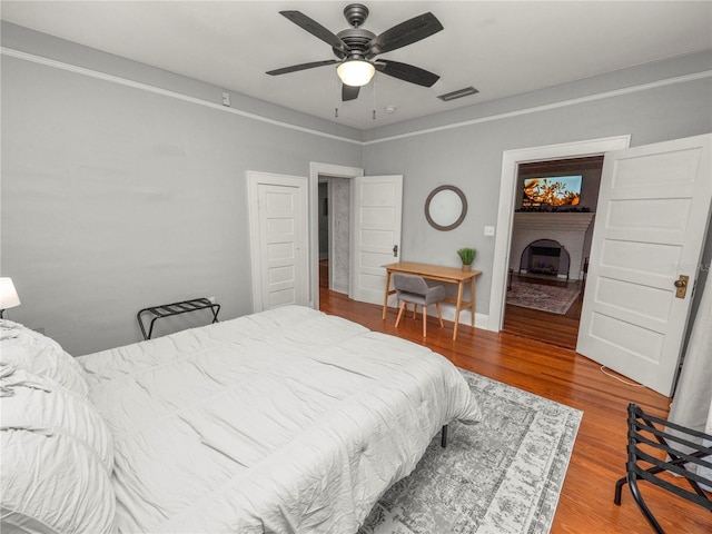 bedroom featuring ceiling fan, visible vents, a fireplace with raised hearth, and wood finished floors