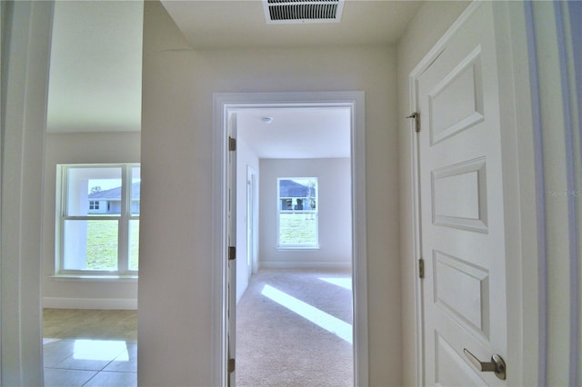 hall with light colored carpet, a healthy amount of sunlight, visible vents, and baseboards