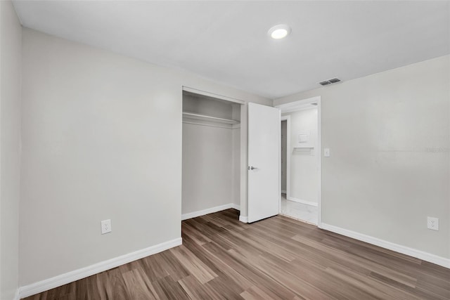 unfurnished bedroom featuring a closet, visible vents, baseboards, and wood finished floors