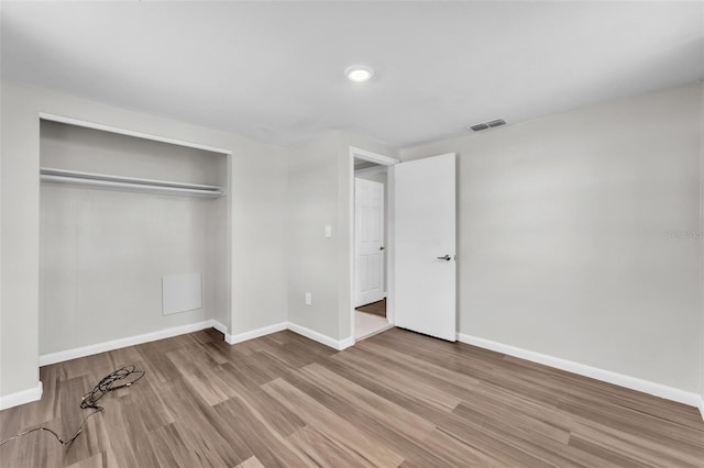 unfurnished bedroom featuring baseboards, a closet, visible vents, and wood finished floors