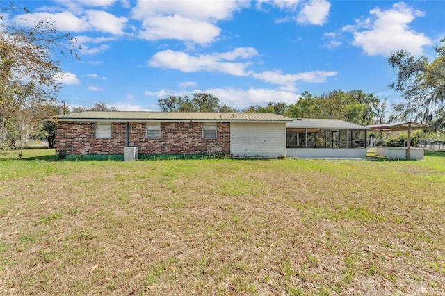 back of property with a sunroom, brick siding, and a yard