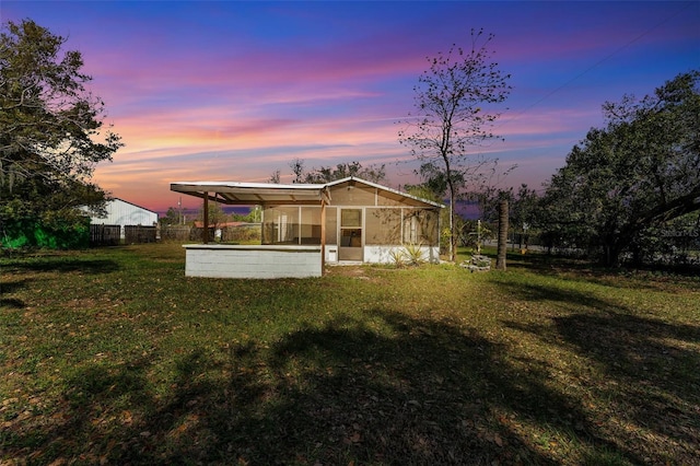 back of property at dusk with a yard, fence, and a sunroom