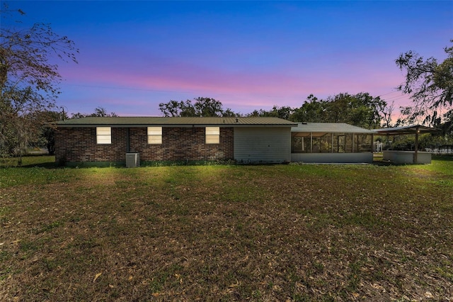 view of front of house featuring brick siding, central AC, a front lawn, and a sunroom