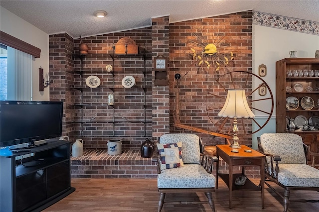 sitting room with lofted ceiling, brick wall, a textured ceiling, and wood finished floors