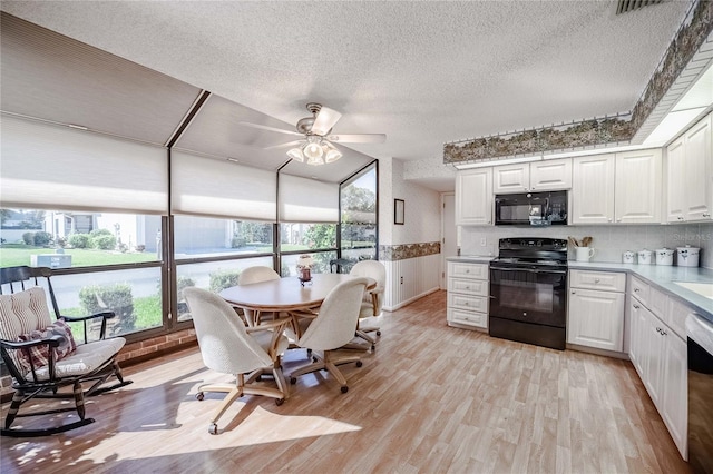 kitchen with a textured ceiling, light wood-style flooring, white cabinetry, light countertops, and black appliances