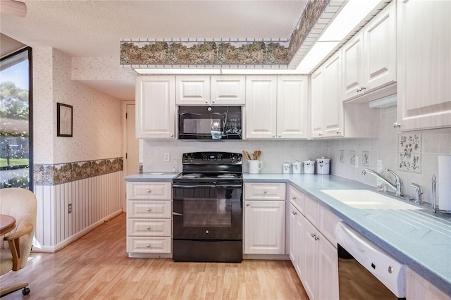 kitchen with a sink, light wood-type flooring, wainscoting, black appliances, and wallpapered walls