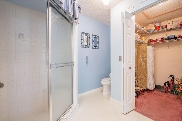 full bathroom featuring a spacious closet, toilet, a stall shower, a textured ceiling, and baseboards