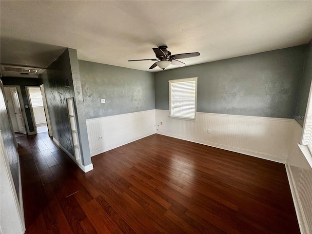 unfurnished room featuring dark wood-style floors, ceiling fan, and wainscoting