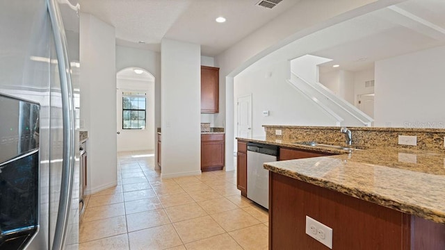 kitchen featuring light tile patterned floors, arched walkways, light stone counters, stainless steel dishwasher, and a sink