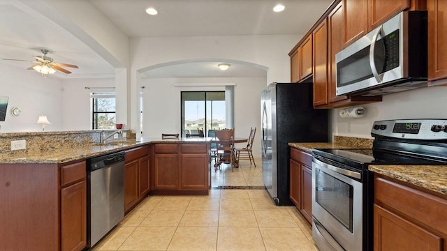 kitchen featuring light stone counters, brown cabinets, light tile patterned floors, stainless steel appliances, and a sink