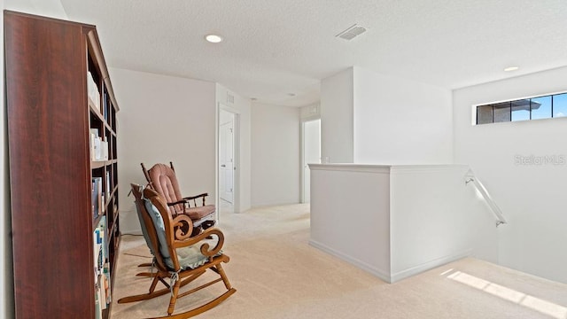 corridor with a textured ceiling, recessed lighting, light colored carpet, visible vents, and an upstairs landing