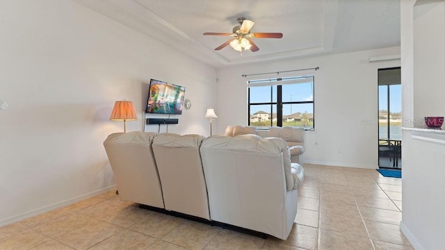 living room with light tile patterned floors, ceiling fan, baseboards, and a raised ceiling