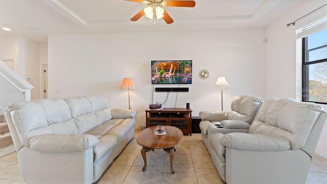 living area with light tile patterned floors, ceiling fan, and a tray ceiling