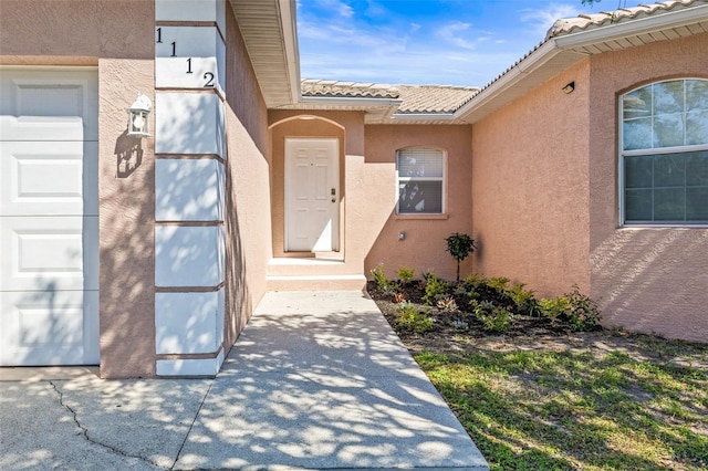 view of exterior entry featuring a garage, a tile roof, and stucco siding