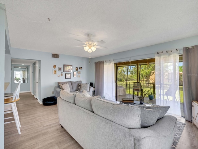 living area with visible vents, light wood-style flooring, a textured ceiling, baseboards, and ceiling fan