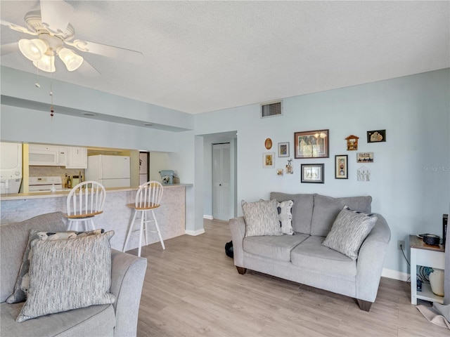 living room with light wood-type flooring, visible vents, baseboards, and a textured ceiling