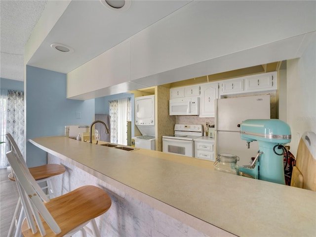 kitchen featuring stacked washer and dryer, a sink, white appliances, white cabinets, and light countertops