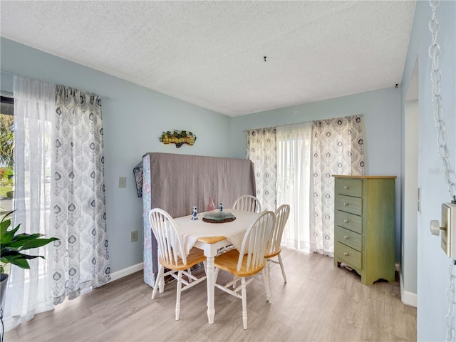 dining area featuring light wood finished floors, a textured ceiling, and baseboards