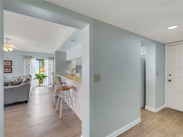 hall with baseboards, a textured ceiling, and light wood finished floors