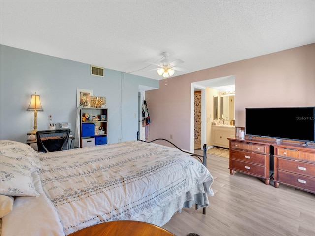 bedroom featuring wood finished floors, visible vents, ensuite bath, ceiling fan, and a textured ceiling