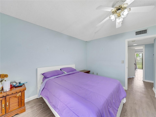 bedroom with wood finished floors, visible vents, baseboards, ceiling fan, and a textured ceiling