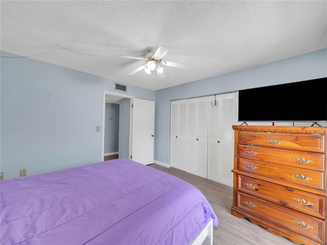 bedroom with visible vents, light wood-style flooring, a textured ceiling, a closet, and ceiling fan