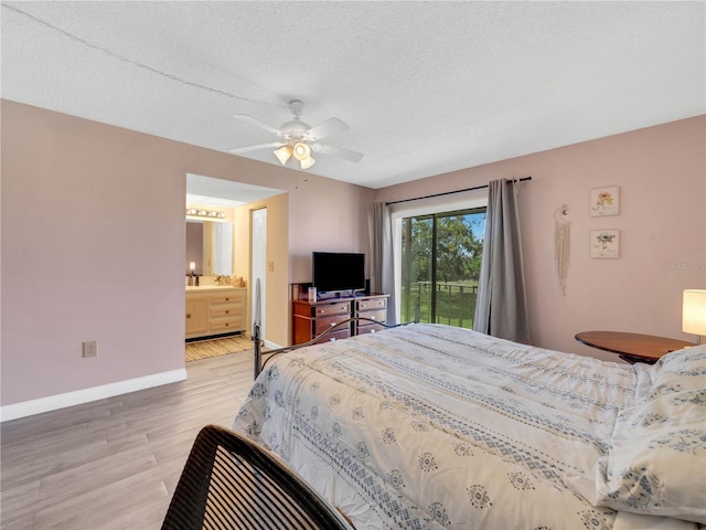 bedroom featuring baseboards, light wood-style flooring, a textured ceiling, ensuite bath, and a ceiling fan