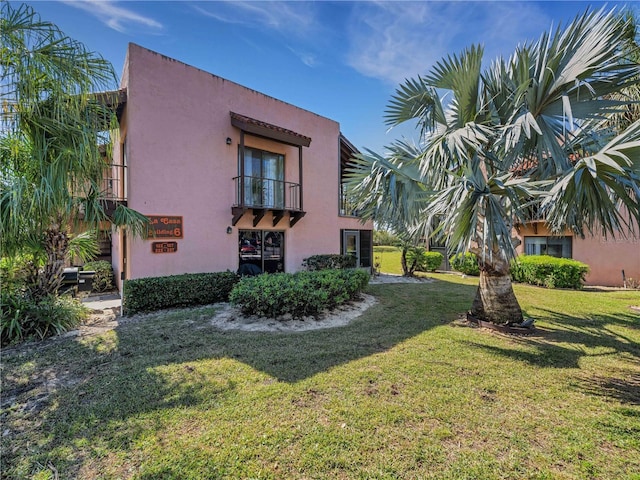 view of side of property with a balcony, stucco siding, and a yard