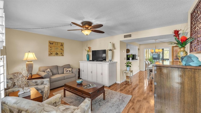 living area with baseboards, visible vents, a ceiling fan, a textured ceiling, and light wood-style floors