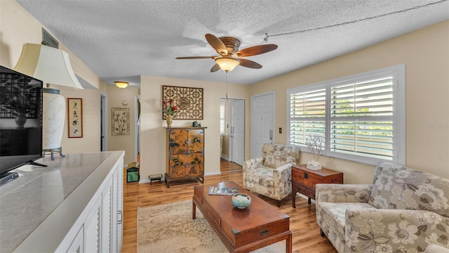 living area featuring ceiling fan, a textured ceiling, and light wood finished floors