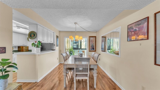 dining area featuring light wood-type flooring, baseboards, a chandelier, and a textured ceiling