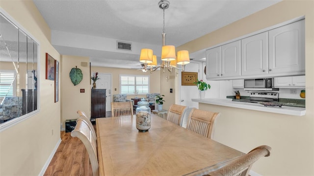 dining area featuring a textured ceiling, light wood-style flooring, a notable chandelier, visible vents, and baseboards