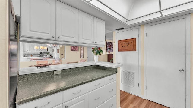 kitchen with light wood-style flooring, dark countertops, visible vents, and white cabinets