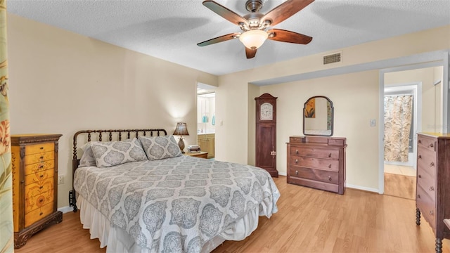 bedroom with light wood-style floors, visible vents, a textured ceiling, and ensuite bath