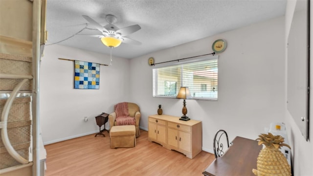 living area with a textured ceiling, ceiling fan, light wood finished floors, and baseboards