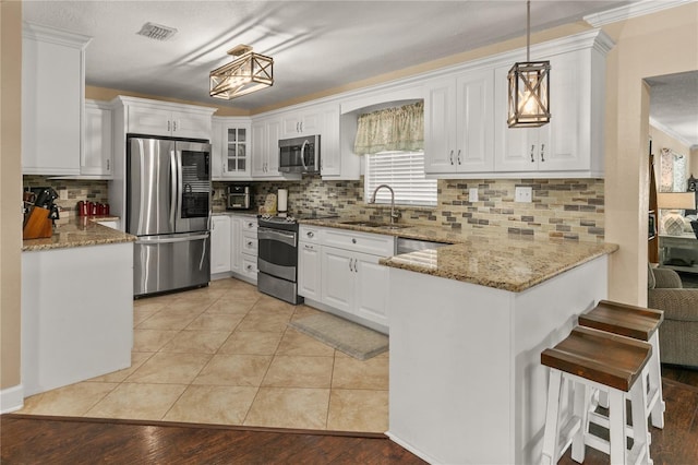 kitchen featuring stainless steel appliances, a peninsula, a sink, visible vents, and light stone countertops