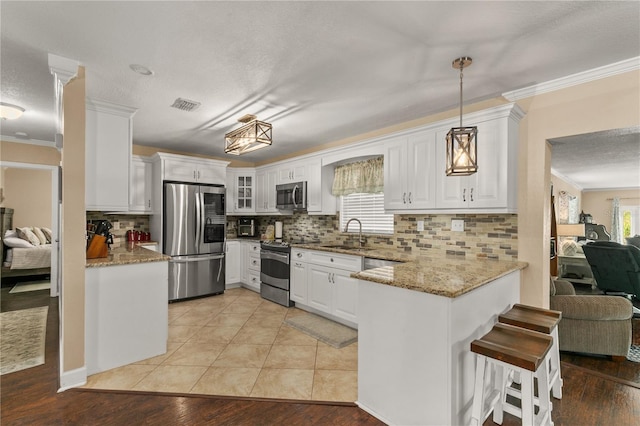 kitchen featuring appliances with stainless steel finishes, ornamental molding, white cabinets, a sink, and a peninsula