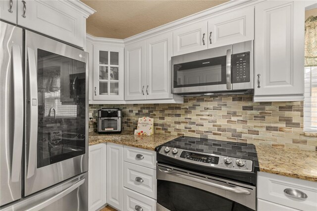 kitchen featuring glass insert cabinets, appliances with stainless steel finishes, white cabinets, and decorative backsplash