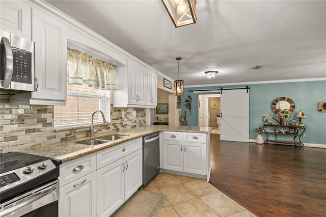 kitchen featuring a barn door, appliances with stainless steel finishes, ornamental molding, white cabinetry, and a sink