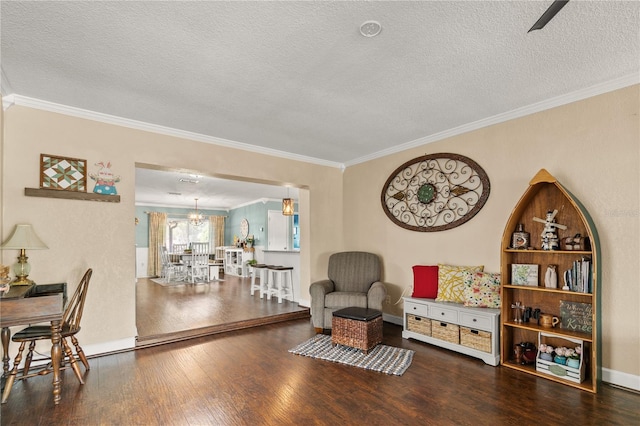 living area featuring a textured ceiling, a chandelier, baseboards, ornamental molding, and wood-type flooring