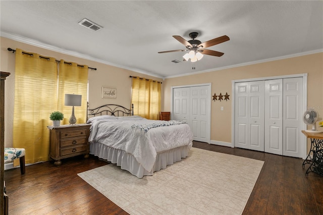 bedroom with multiple closets, dark wood-style flooring, visible vents, and crown molding