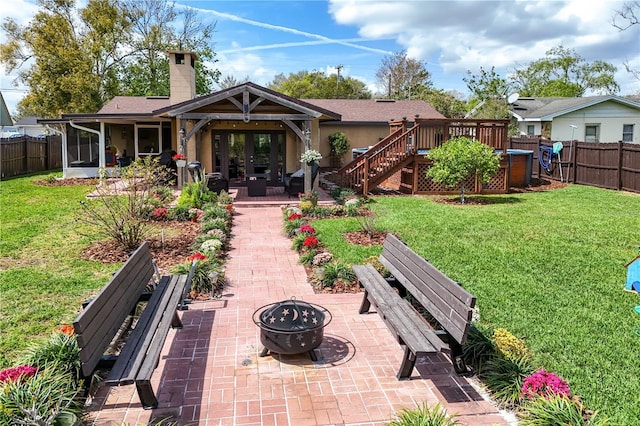 back of house featuring french doors, an outdoor fire pit, a fenced backyard, and a lawn