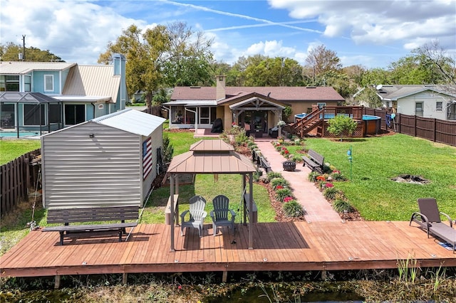 rear view of property featuring an outdoor fire pit, a lawn, a fenced backyard, a deck, and a gazebo