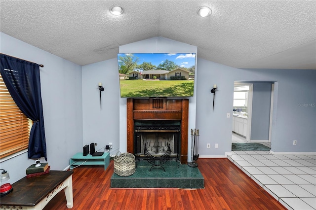 unfurnished living room with lofted ceiling, a fireplace with raised hearth, a textured ceiling, and wood finished floors