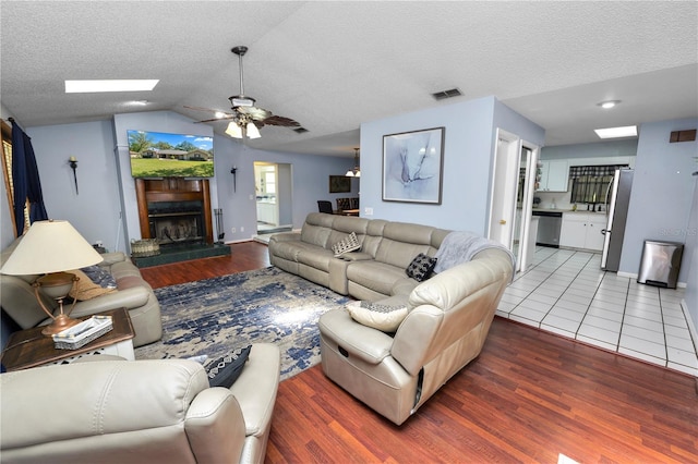 living area featuring a fireplace, visible vents, lofted ceiling with skylight, a textured ceiling, and wood finished floors