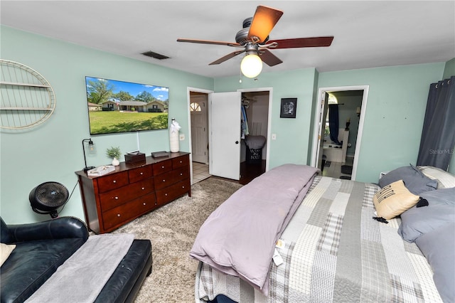 bedroom featuring ceiling fan, light colored carpet, visible vents, a spacious closet, and ensuite bath